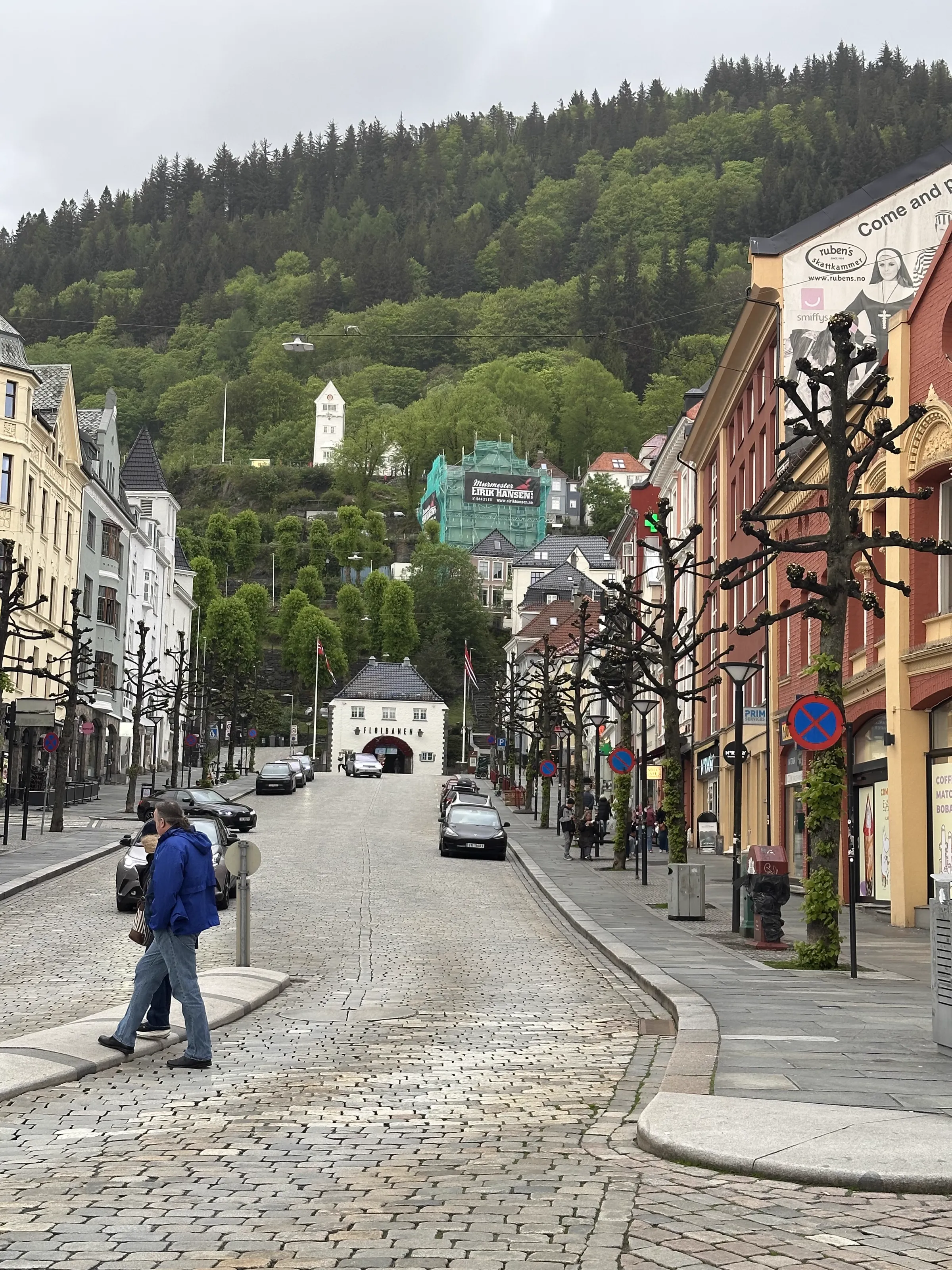 A quiet cobblestone street in Bergen with colourful buildings on either side and a mountain view in the background