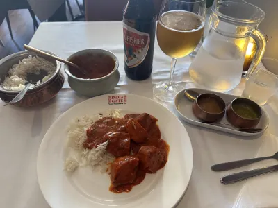A plate of butter chicken curry served with a cold beer