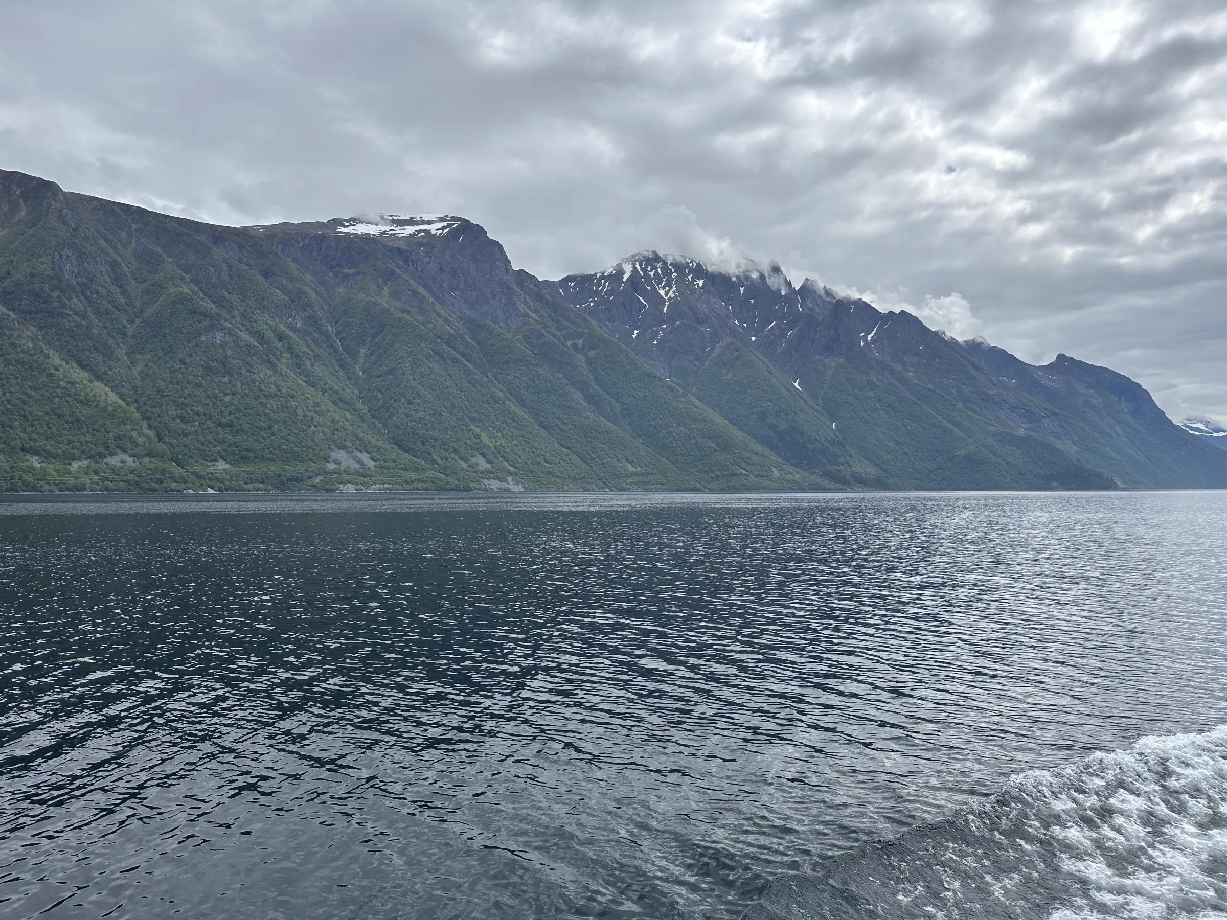 Calm fjord waters stretching into the distance with steep mountain slope rising into the clouds