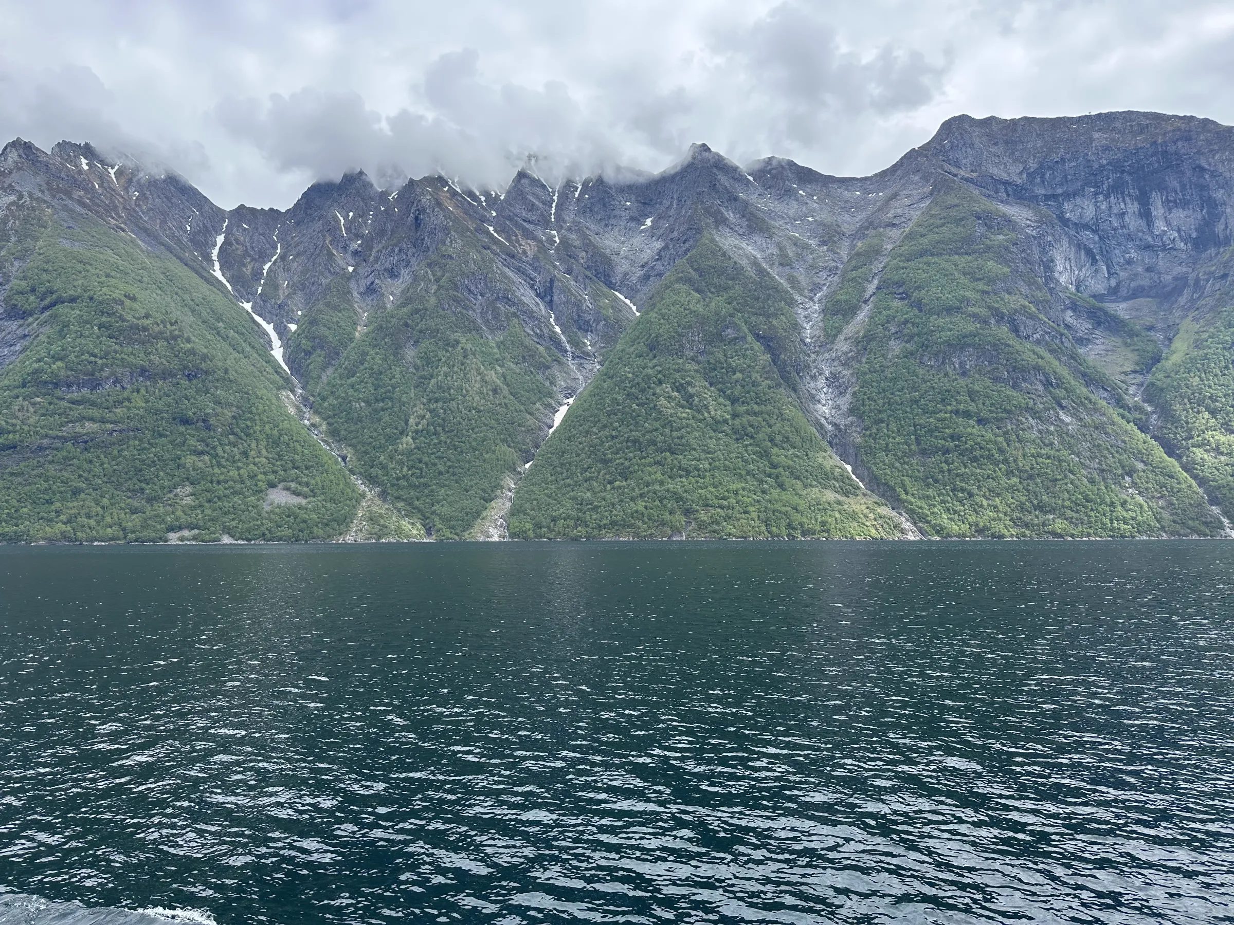 Ragged, steep cliff face with waterfalls running into the fjord