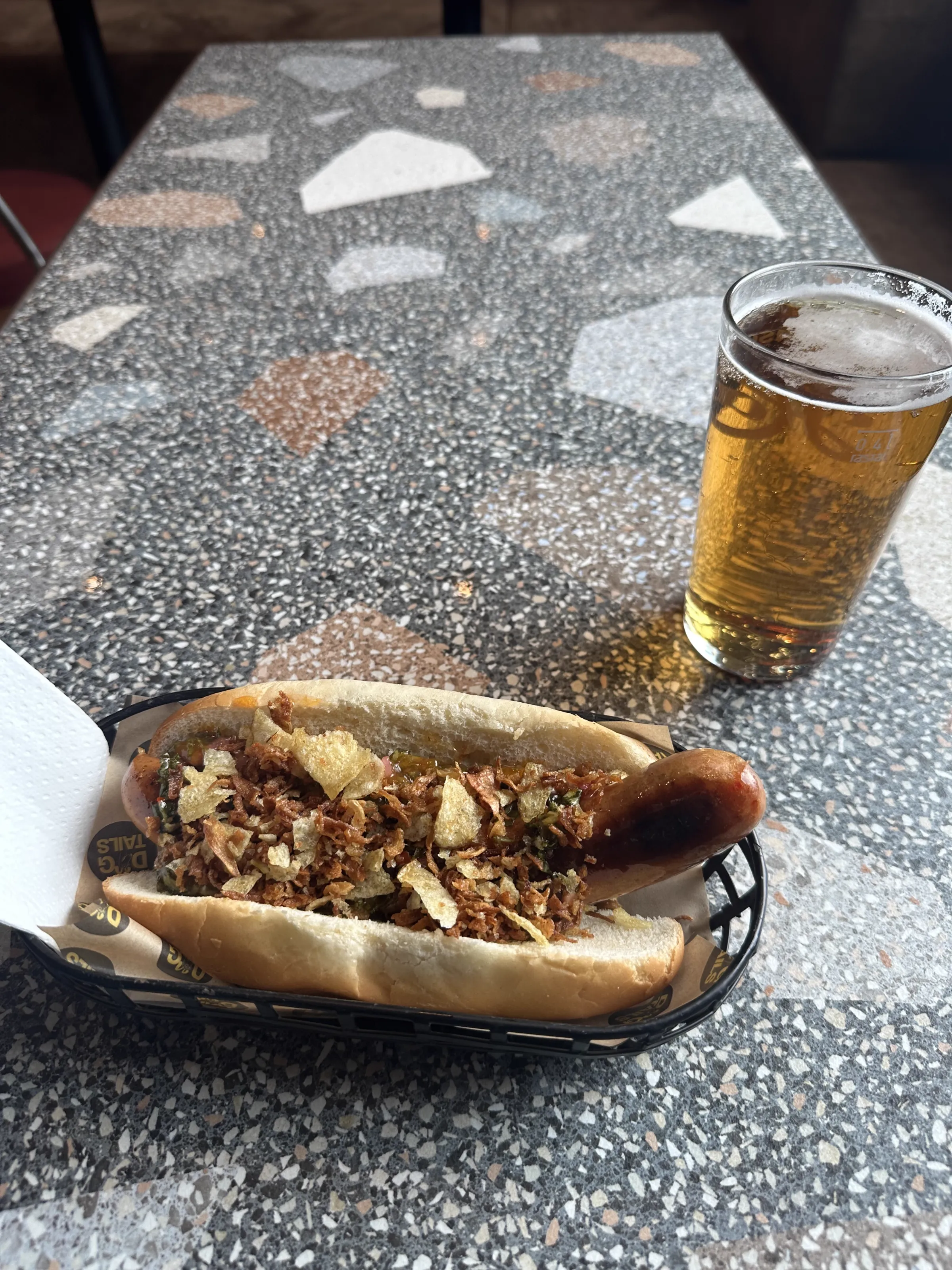 A loaded Norwegian hotdog served alongside a cold beer