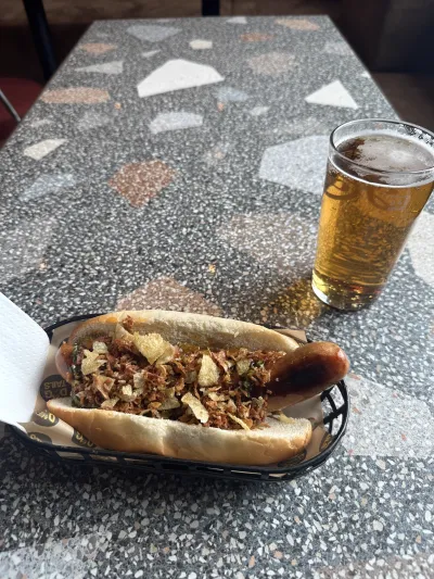 A loaded Norwegian hotdog served alongside a cold beer